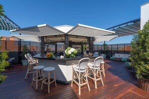 A deck with a bar area, wicker chairs, and a sofa. - NH Collection Valencia Colón (Valencia)