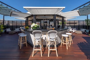 Un área de bar con terraza de madera, sillas de mimbre y barra.