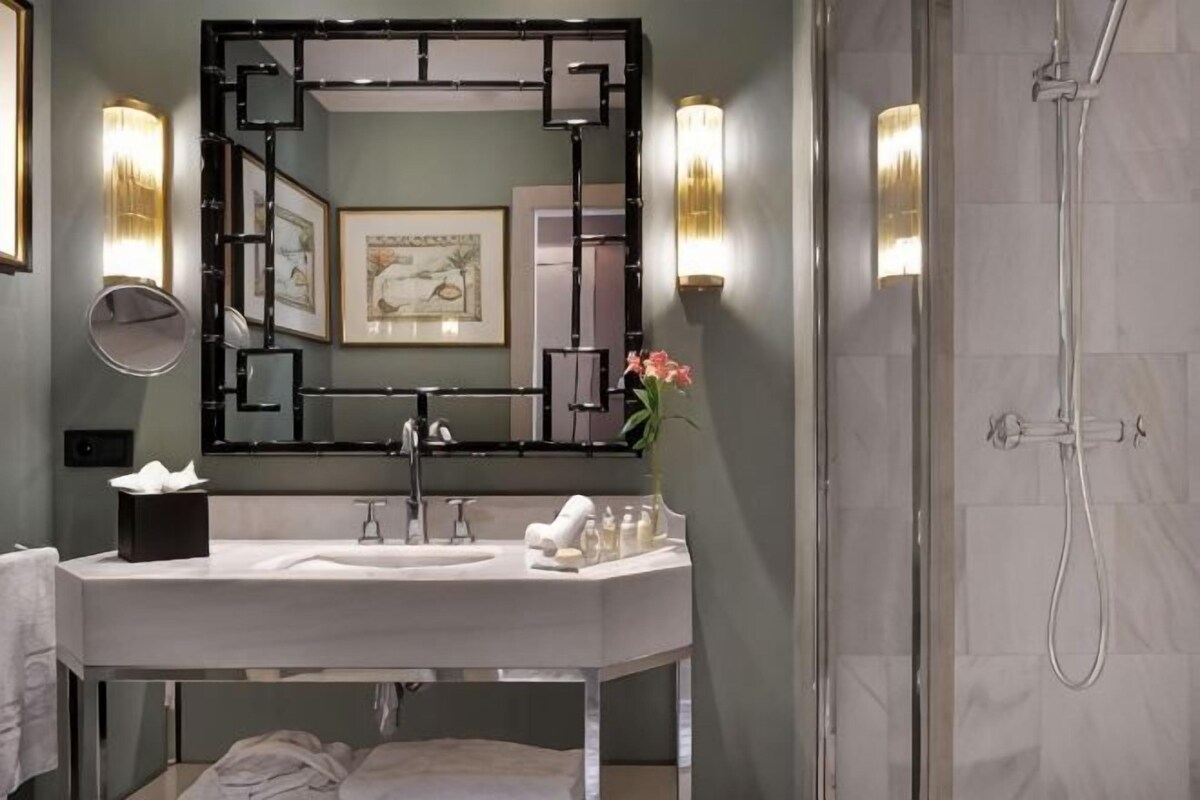 Un baño moderno con un espejo grande, apliques de pared, ducha y lavamanos con artículos de aseo.