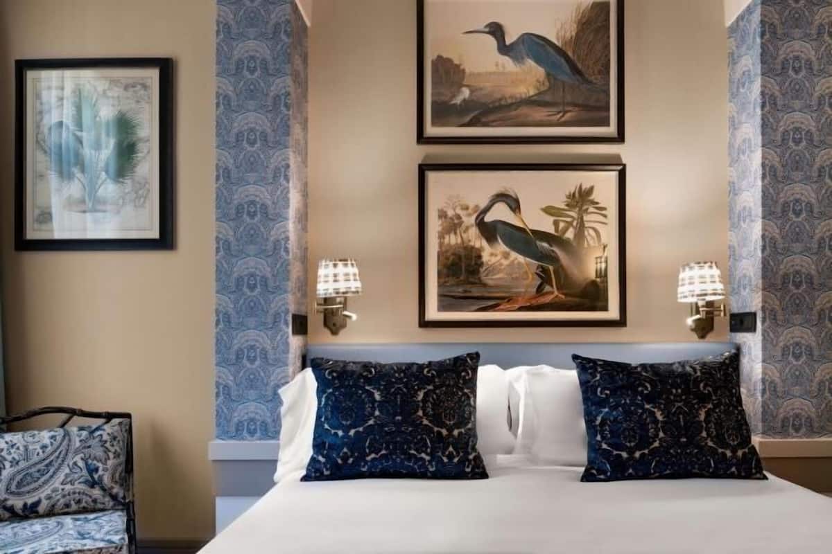 A hotel room with a bed, two wall-mounted lamps, and two framed bird paintings.