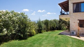 Un bâtiment en pierre de deux étages, doté d’un balcon, entouré d’une végétation bien entretenue et surplombant un ciel dégagé.