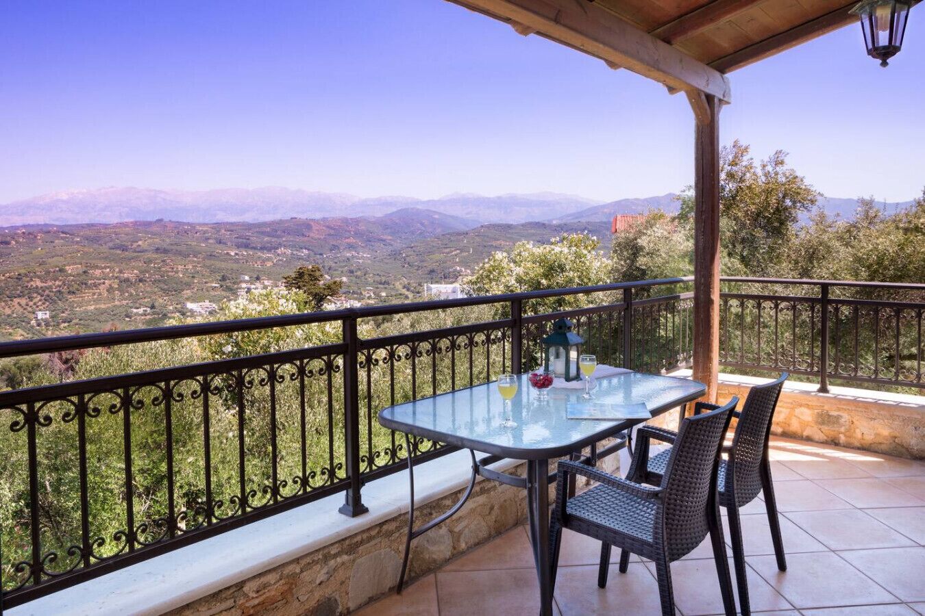 A balcony with a table and chairs, a stone wall, and a view of distant mountains.