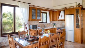 Une cuisine avec des meubles de rangement en bois, une table à manger avec des chaises, un réfrigérateur et une fenêtre avec des rideaux.