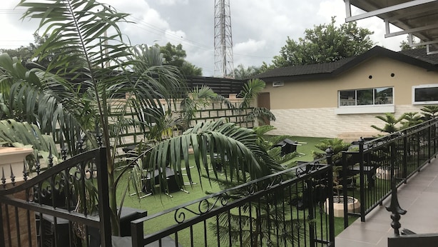 Un balcon donnant sur un jardin aménagé, un bâtiment avec un toit en tuiles et, au loin, une haute tour de communication.
