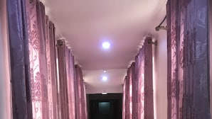 Un couloir avec des rideaux à motifs, un sol en marbre et un luminaire au plafond.
