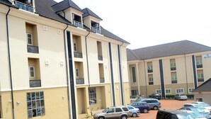 Un hôtel à plusieurs étages, doté d’une façade beige, de balcons et d’un parking où sont stationnées plusieurs voitures.