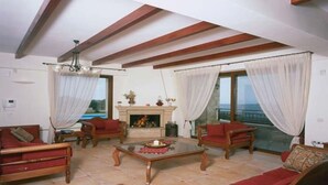 A living room with a fireplace, wooden furniture, and large windows with curtains. - Family Villa w/Pool, Billiard ,Ping Pong, BBQ area (Chania)