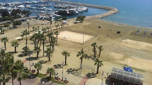 Una marina con imbarcazioni ormeggiate, una spiaggia sabbiosa con palme e una limpida vista sul mare.
