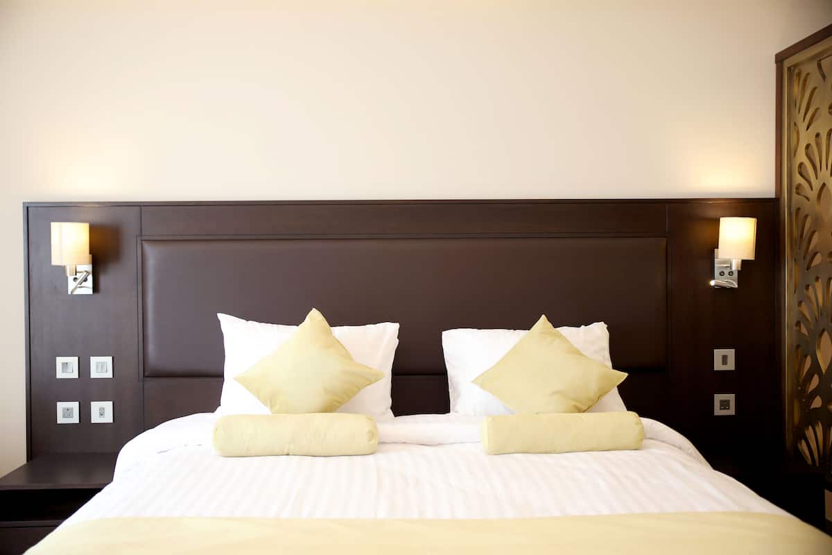 A neatly made bed with white linens and two pillows, a dark headboard, and wall-mounted lights.