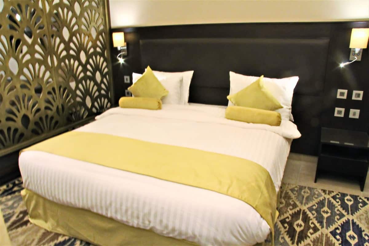 Ein Hotelzimmer mit einem großen Bett, zwei Nachttischen, einem dekorativen Raumteiler und einem gemusterten Teppich.