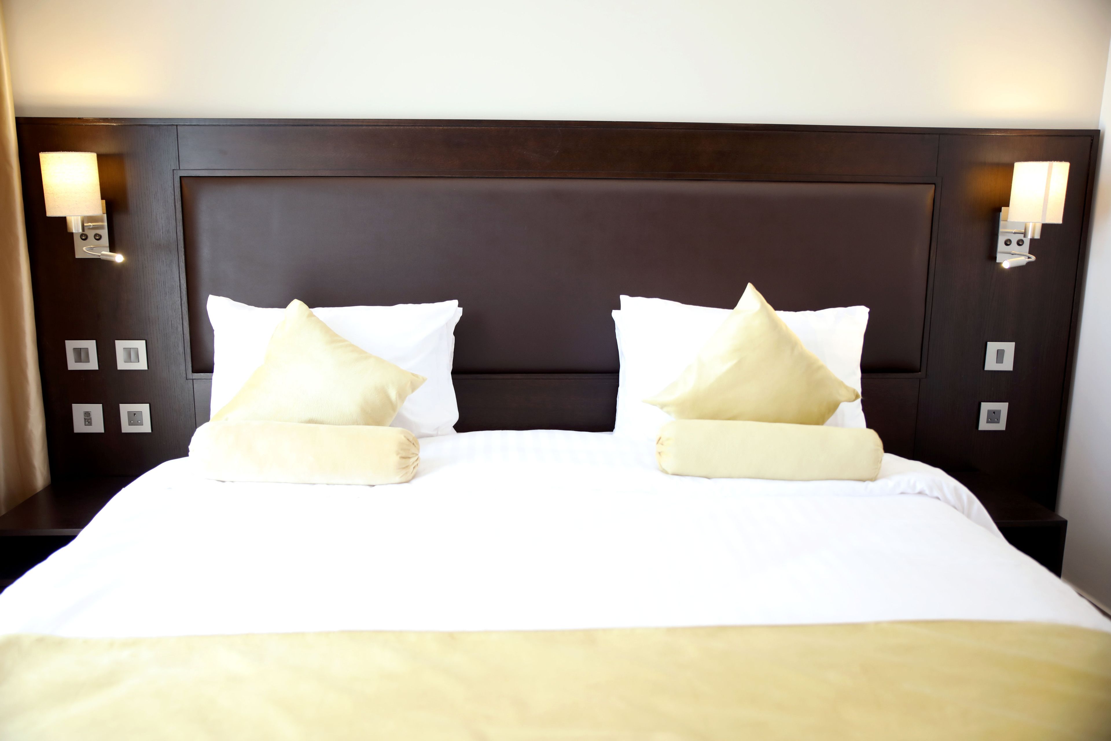 A hotel room with a large bed, two bedside lamps, and a dark headboard.