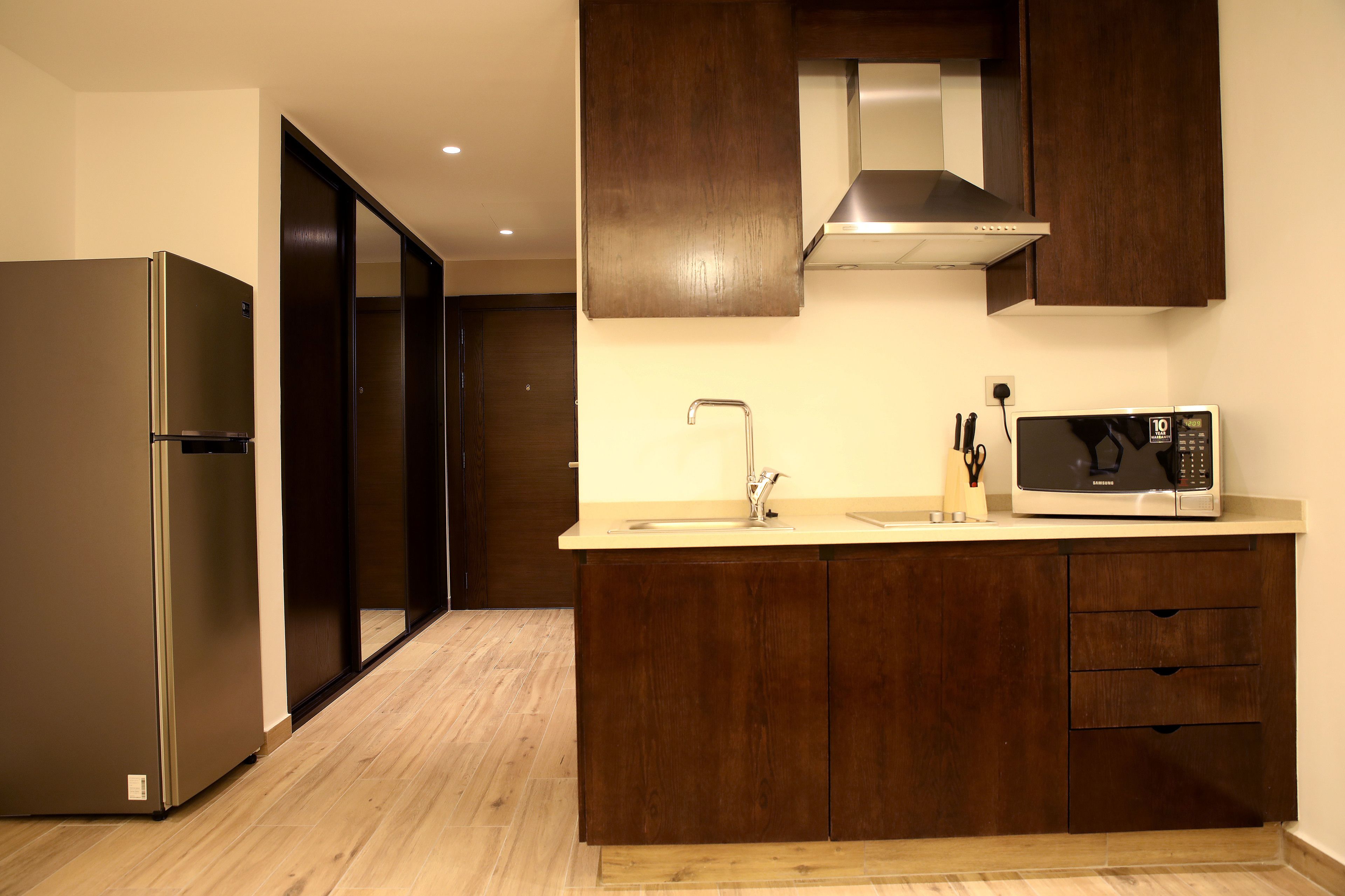 A modern kitchen with a stainless steel refrigerator, a microwave, and wooden cabinets.