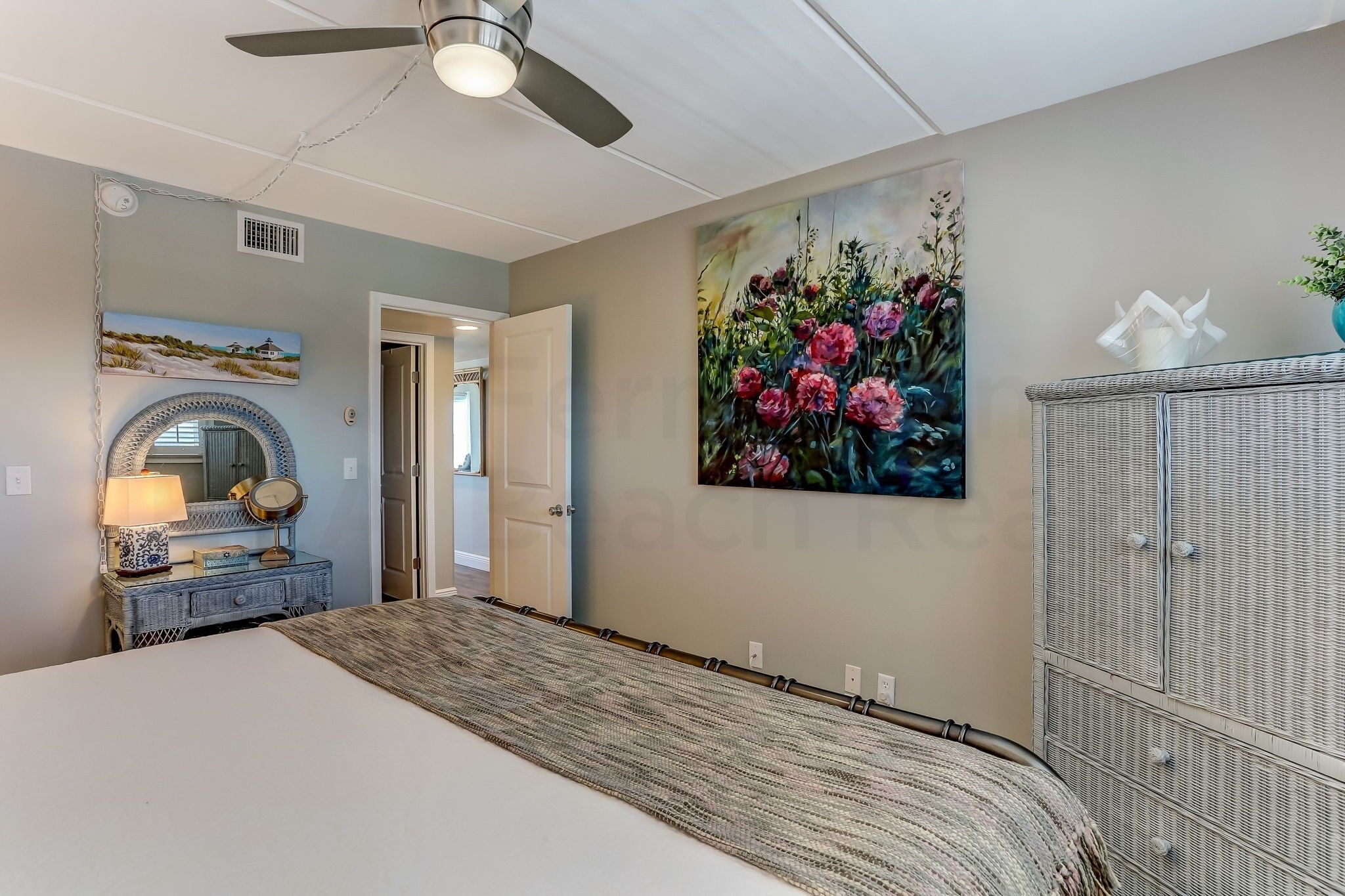 A bedroom with a bed, a ceiling fan, a painting, a dresser, and a cabinet.