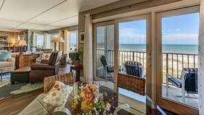Ein geräumiges Wohnzimmer mit einem großen Schiebeglastür, die auf einen Balkon mit Blick auf den Strand führt.