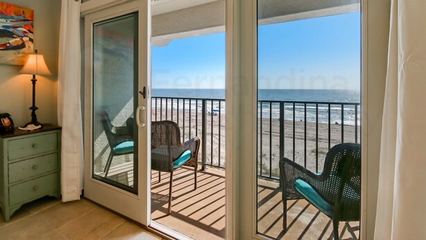 Una habitación con puerta de vidrio corredera que da a un balcón con vista a la playa.