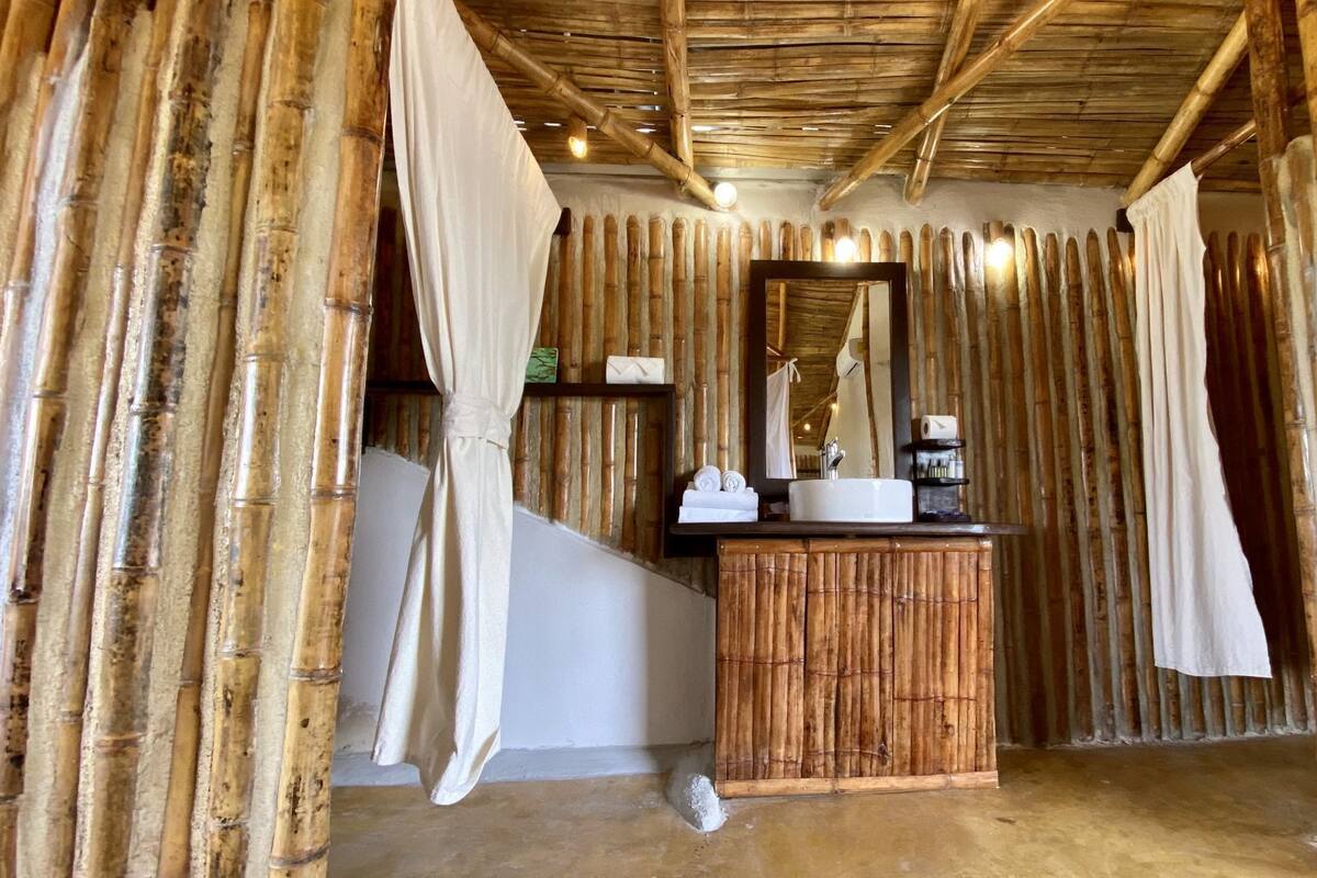 Quarto com parede de bambu, toucador de madeira com espelho e pia branca.