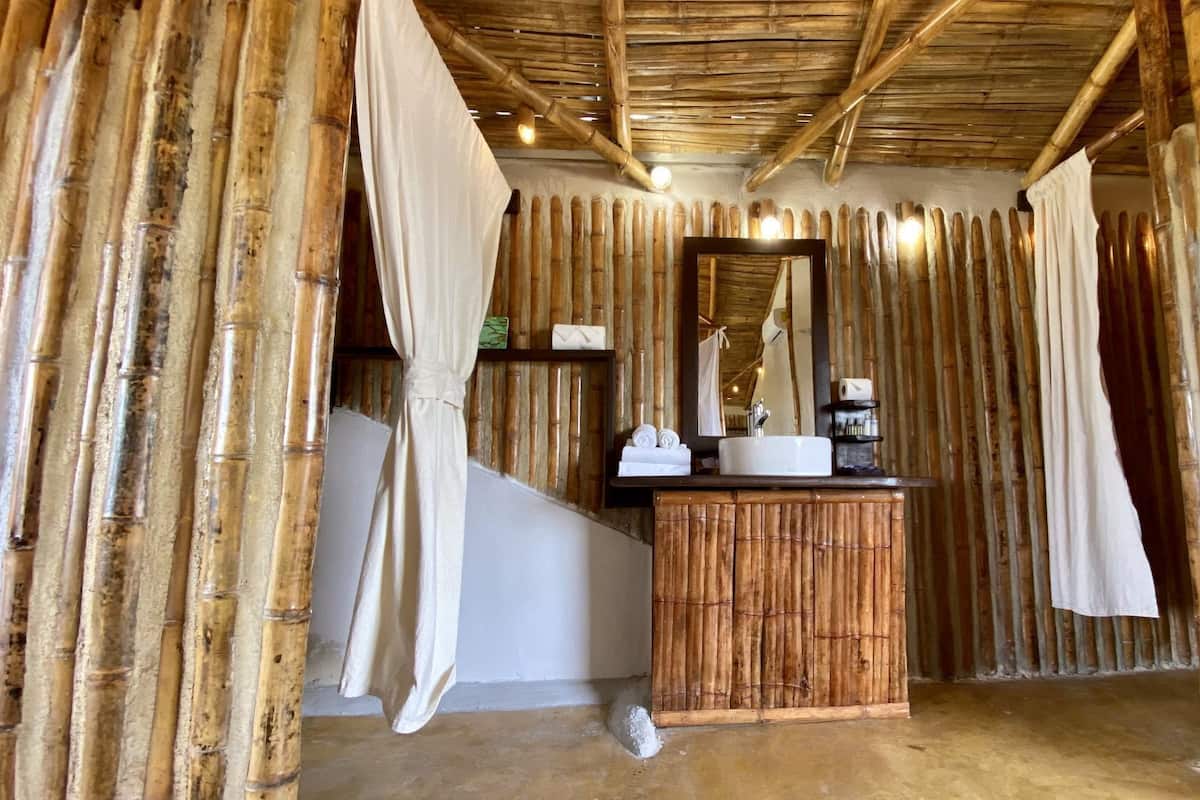 A room with a bamboo wall, a wooden vanity with a mirror, and a white sink.