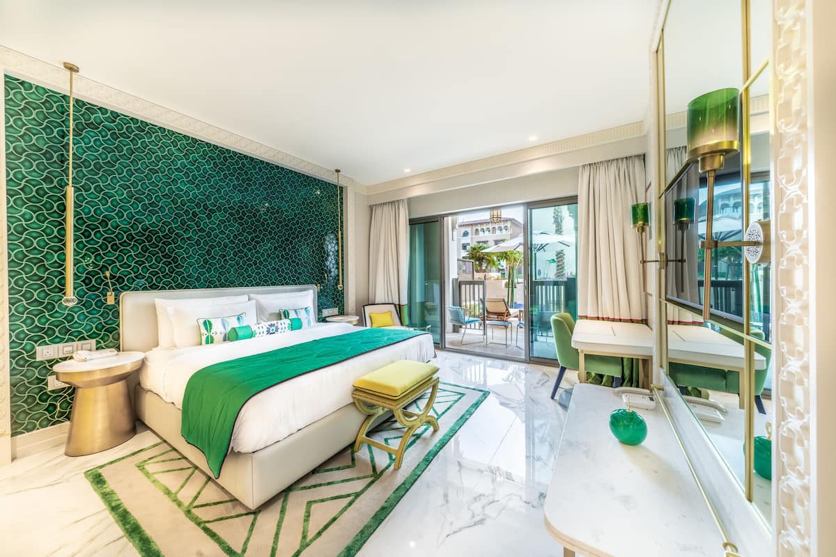 Une chambre d’hôtel moderne dotée d’un grand lit, d’un mur orné d’un motif vert, d’un balcon avec des meubles d’extérieur et d’un sol en marbre.