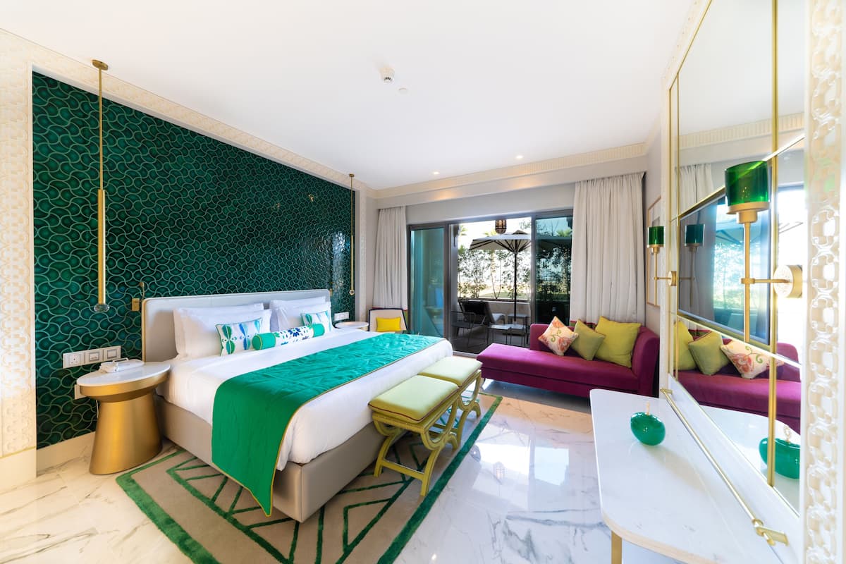 Une chambre d’hôtel moderne dotée d’un grand lit, d’un coin salon avec un canapé, d’une table à manger et d’un balcon avec des sièges d’extérieur.