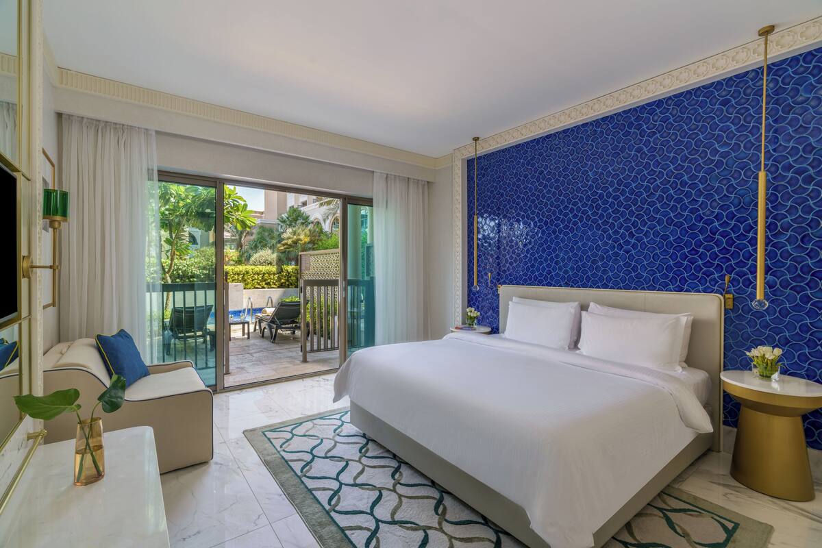Une chambre d’hôtel avec un grand lit, un canapé, une télévision et un balcon aménagé avec du mobilier d’extérieur.