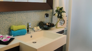 Un baño con lavamanos blanco, un espejo, toallero y zona de ducha.