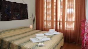 Habitación de hotel con cama, un tapiz decorativo, ventana con cortinas y mesita de noche con toallas.
