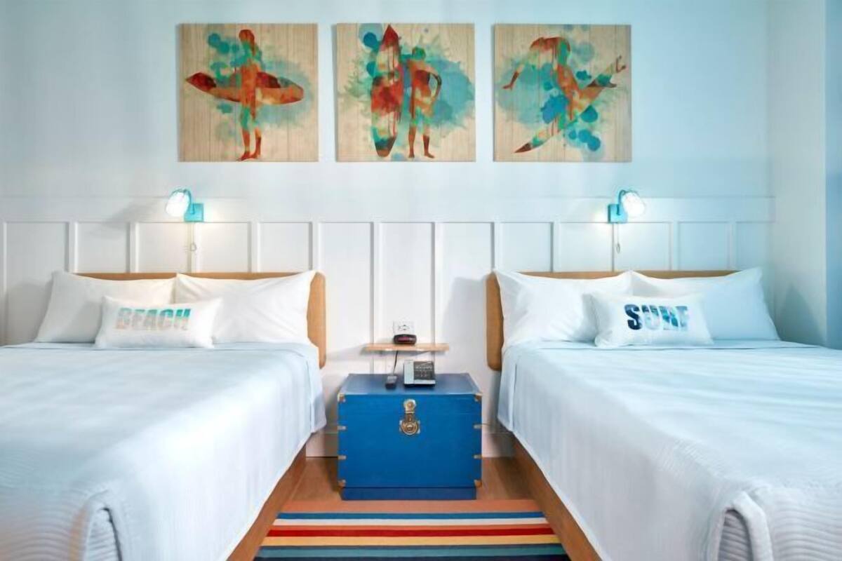 A hotel room with two beds, a blue chest of drawers, and three paintings on the wall.