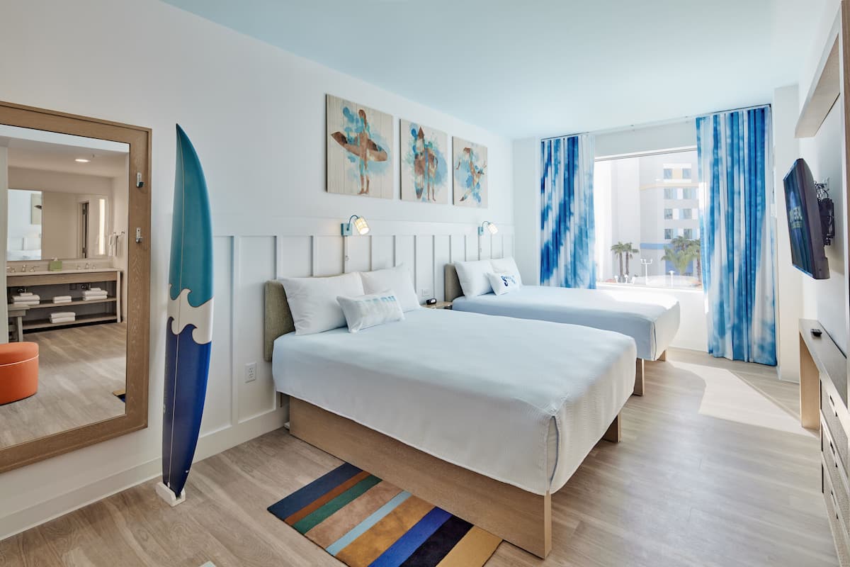 A hotel room with two beds, a large mirror, artwork on the wall, and a view of the outside.