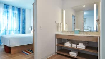 A hotel room with a bed, a bathroom with a sink and mirror, and a shower area.