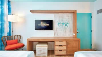 Habitación de hotel con escritorio de madera, televisor, una obra de arte en la pared, puerta y ventana con cortinas.