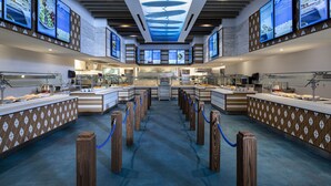 A modern hotel lobby with a central reception desk, multiple screens displaying menus, and a ceiling with a unique design. - Universal's Endless Summer Resort - Surfside Inn and Suites (Orlando)