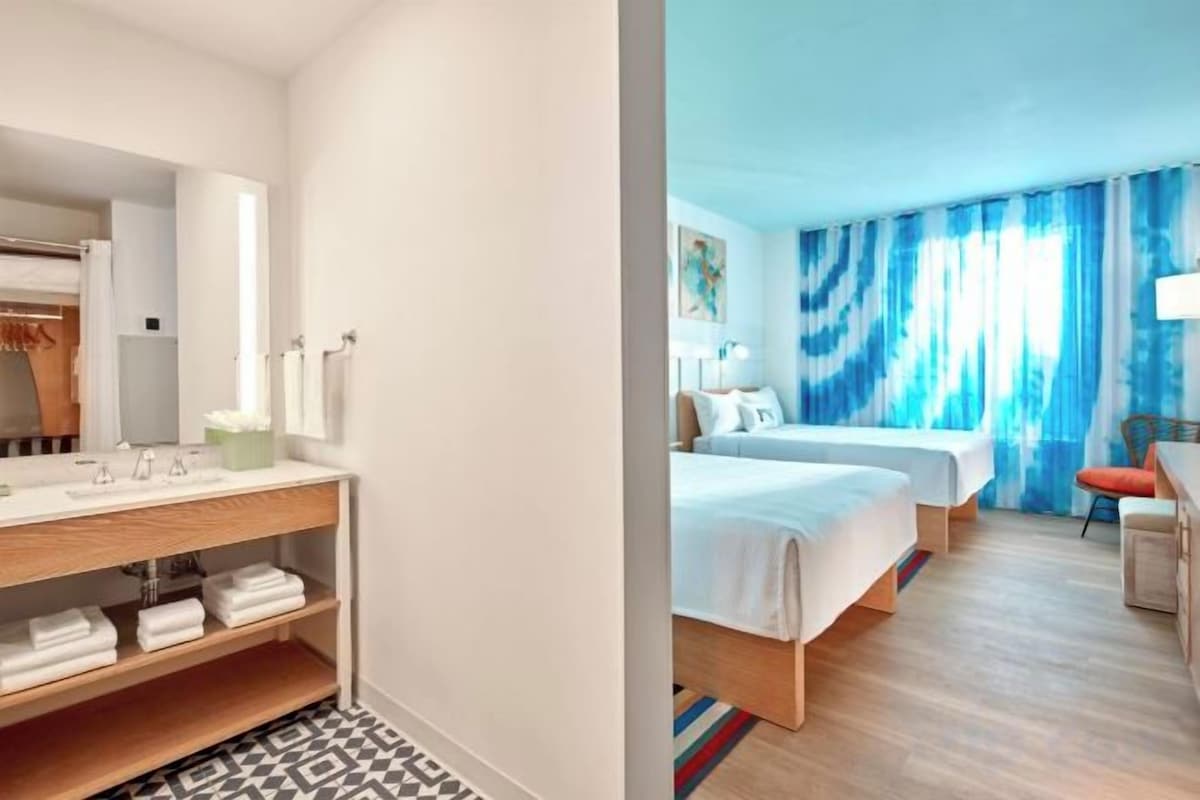 A hotel room with a bed, a bedside table, a chair, and a bathroom with a mirror and sink.