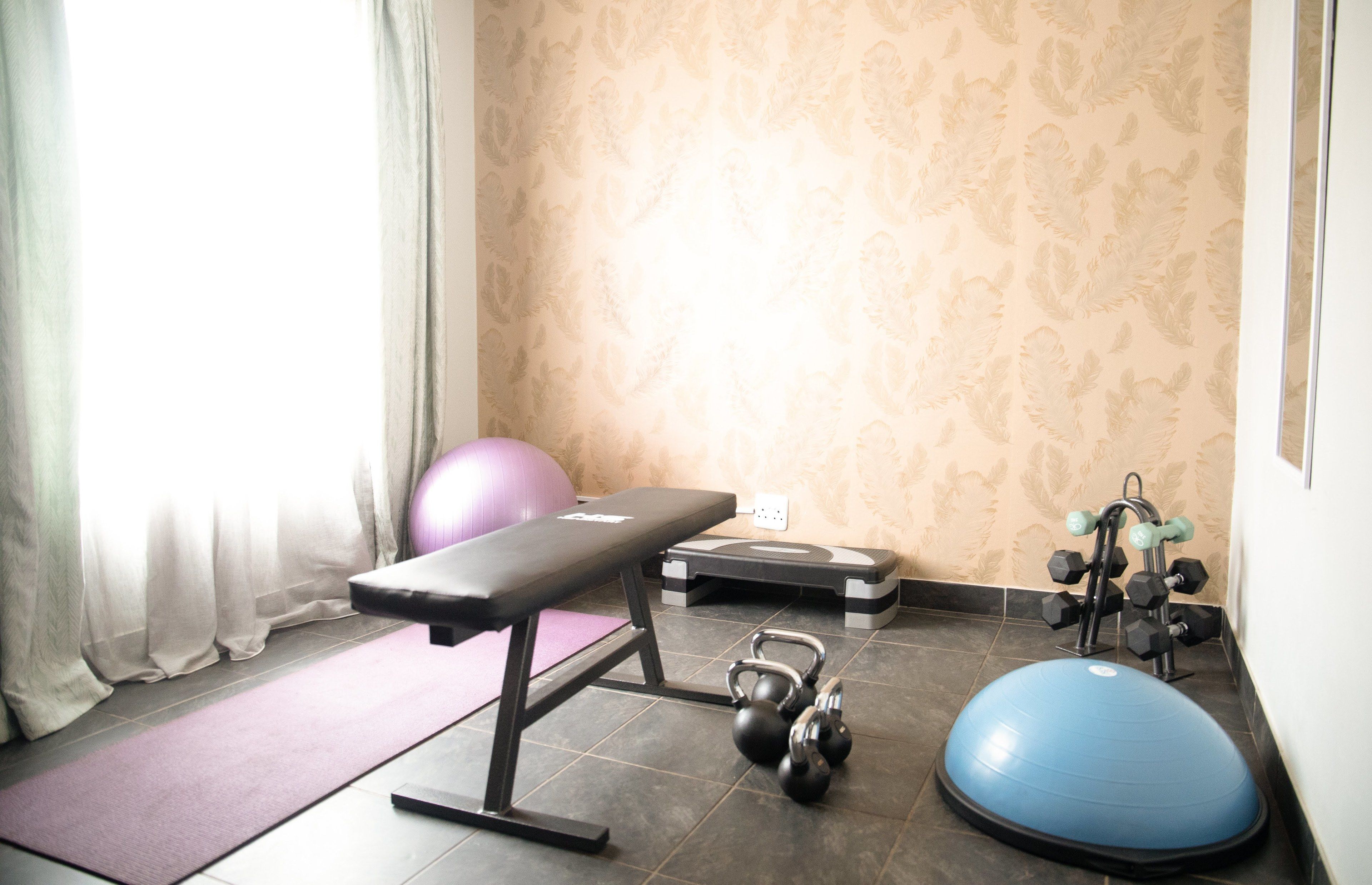 Ein Heim-Fitnessraum mit einer Bank, einem Trainingsball, Kurzhanteln und einer Waage.