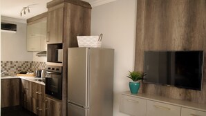 Une cuisine moderne avec des meubles en bois, des appareils en acier inoxydable, un téléviseur à écran plat et une plante en pot.