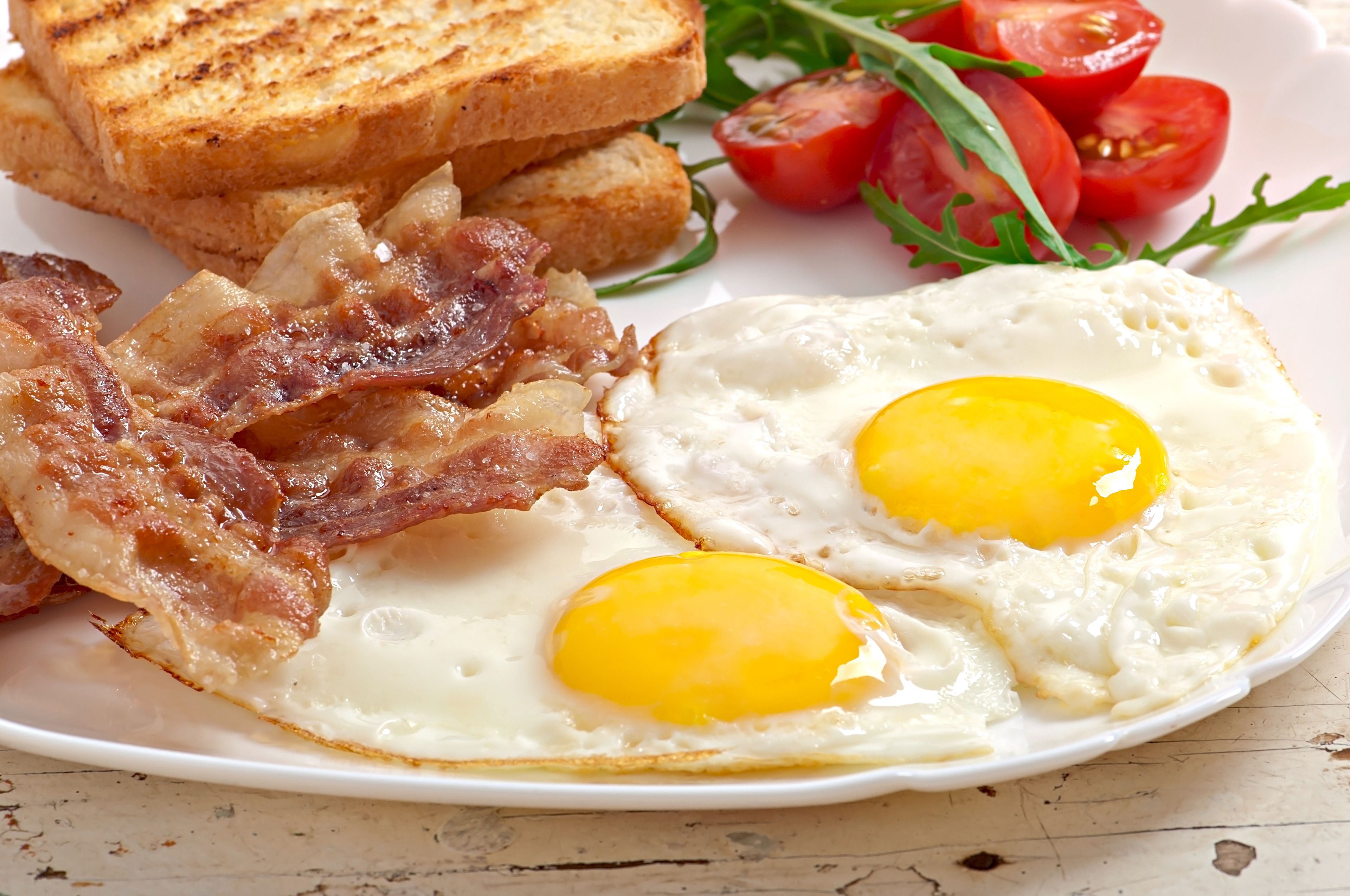 Un plato con huevos fritos, tocino, tostadas y tomates.
