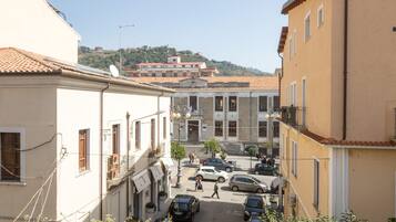 A narrow street with buildings on either side, a few parked cars, and pedestrians.