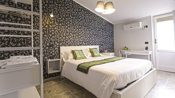 Quarto com cama, mesas de cabeceira brancas, escrivaninha e guarda-roupa.