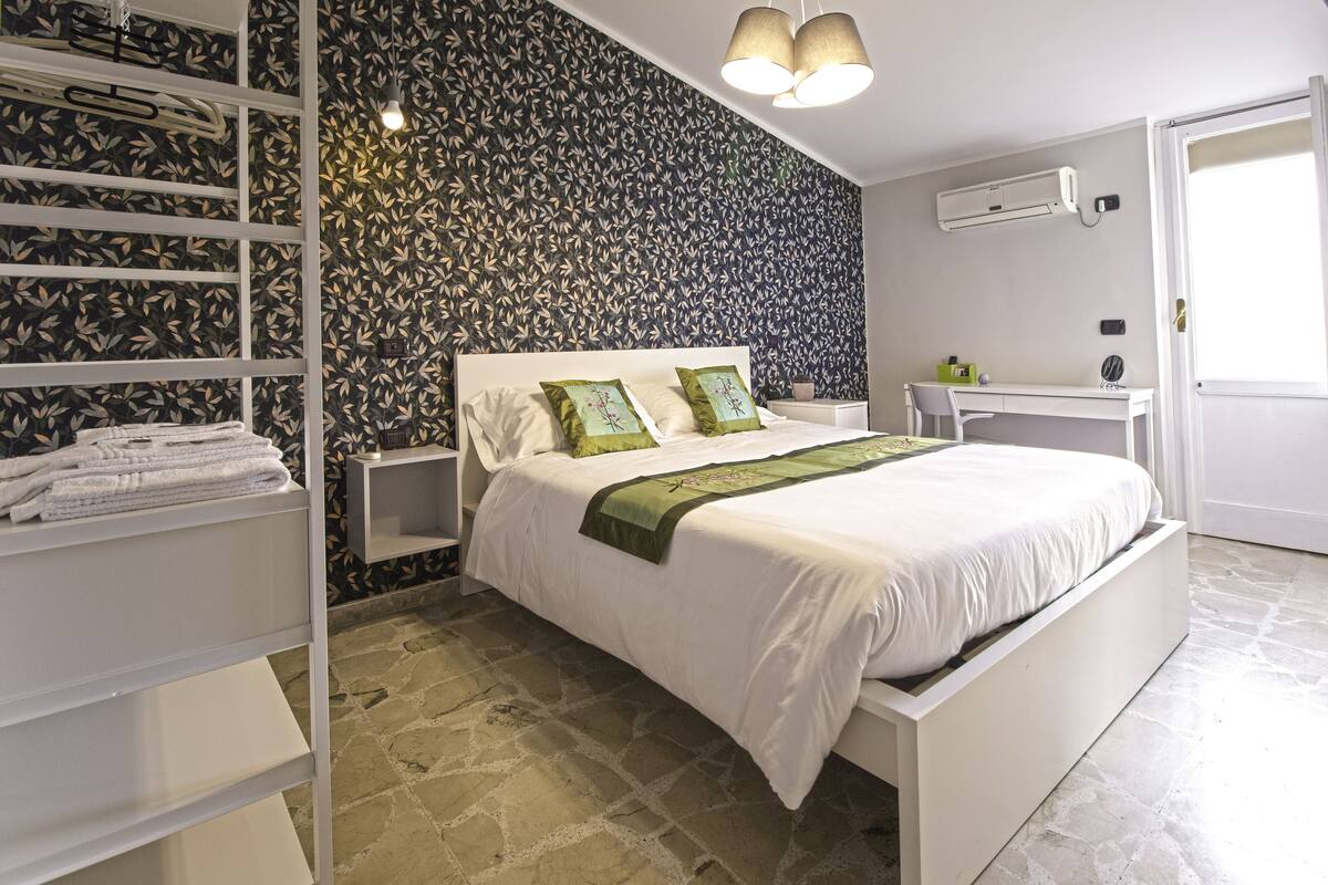 Une chambre à coucher avec un lit, deux tables de chevet blanches, un bureau et une armoire.