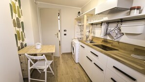 Uma cozinha compacta com bancada de madeira, armários brancos, máquina de lavar e um pequeno espaço de refeições com uma cadeira.