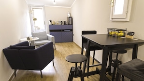 Um espaço de estar compacto com sofá, uma pequena mesa redonda, uma mesa de jantar com banquetas, uma cozinha compacta e uma janela com vista.