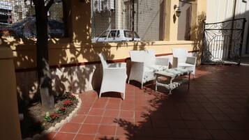 An outdoor patio with white wicker furniture, a tiled floor, and a view of a street with a car.