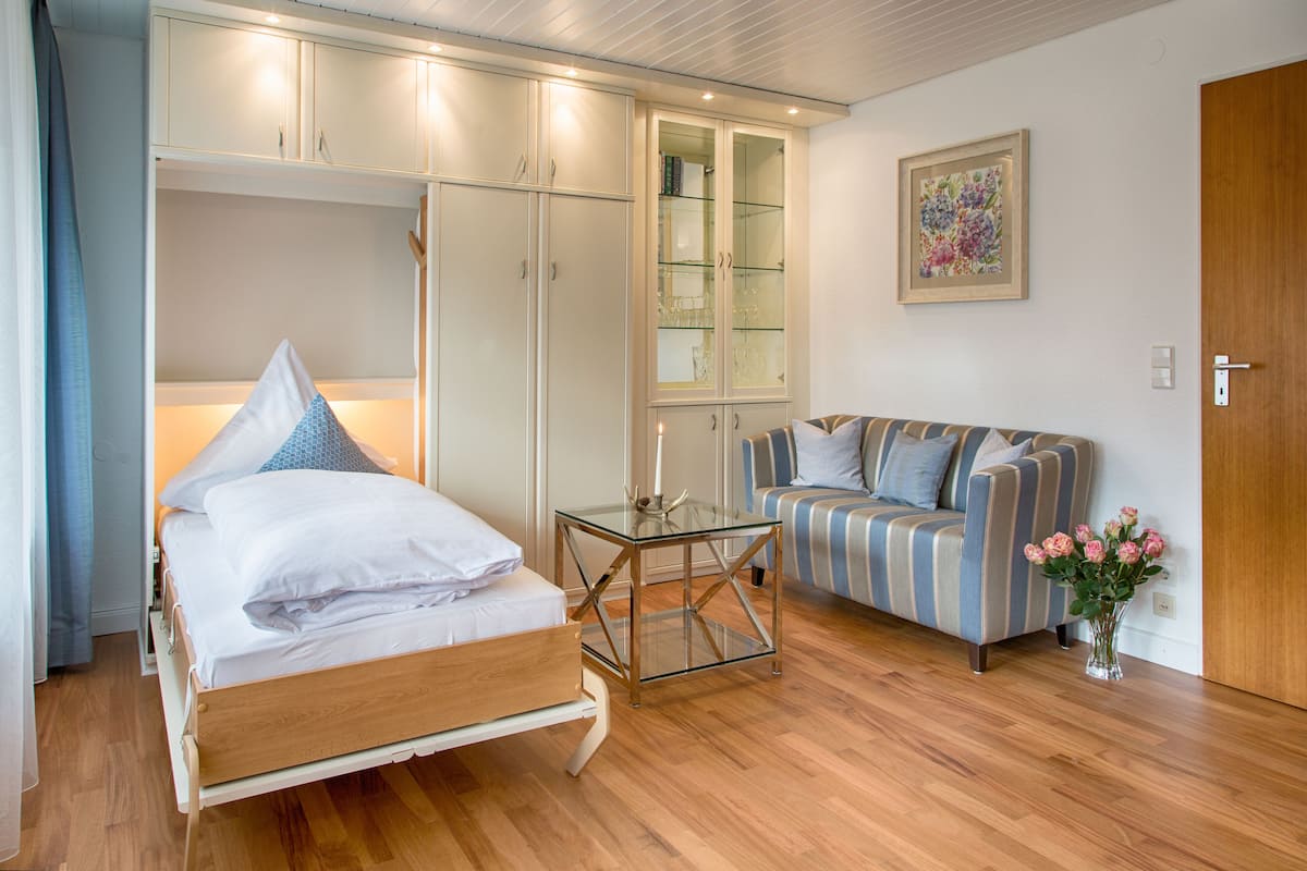 Un dormitorio con cama, una mesa de vidrio, un sofá a rayas, un armario y un cuadro en la pared.