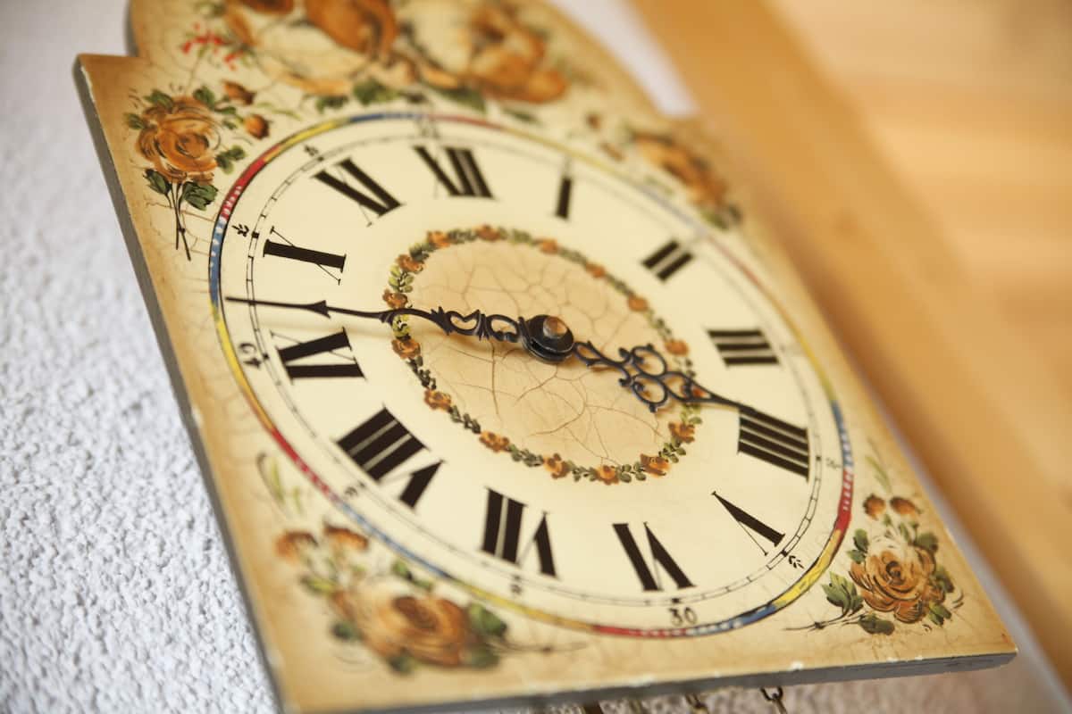 Un reloj de pared con diseño floral y números romanos.