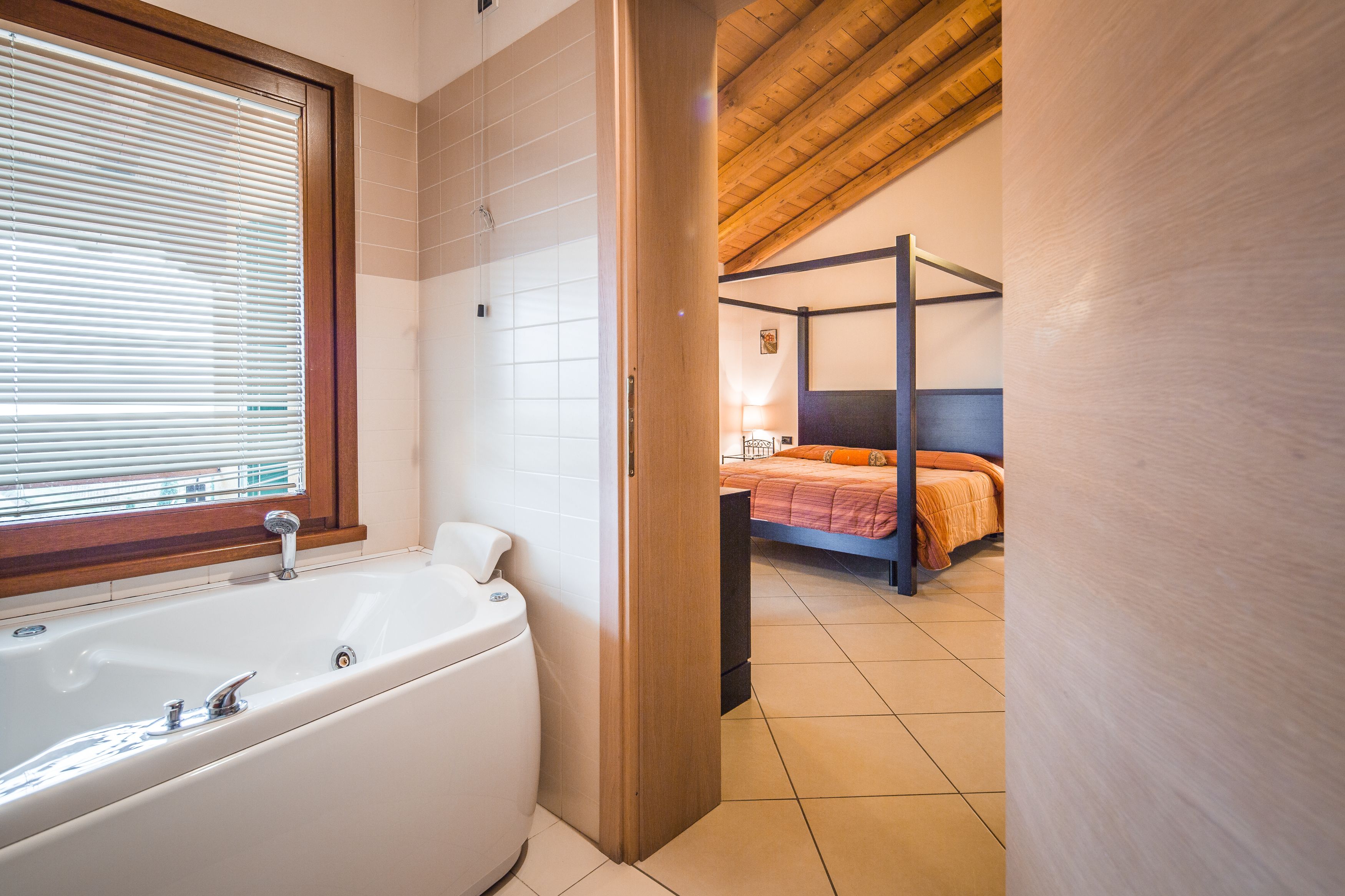 Un bagno con una vasca, una finestra con persiane e un soffitto in legno.