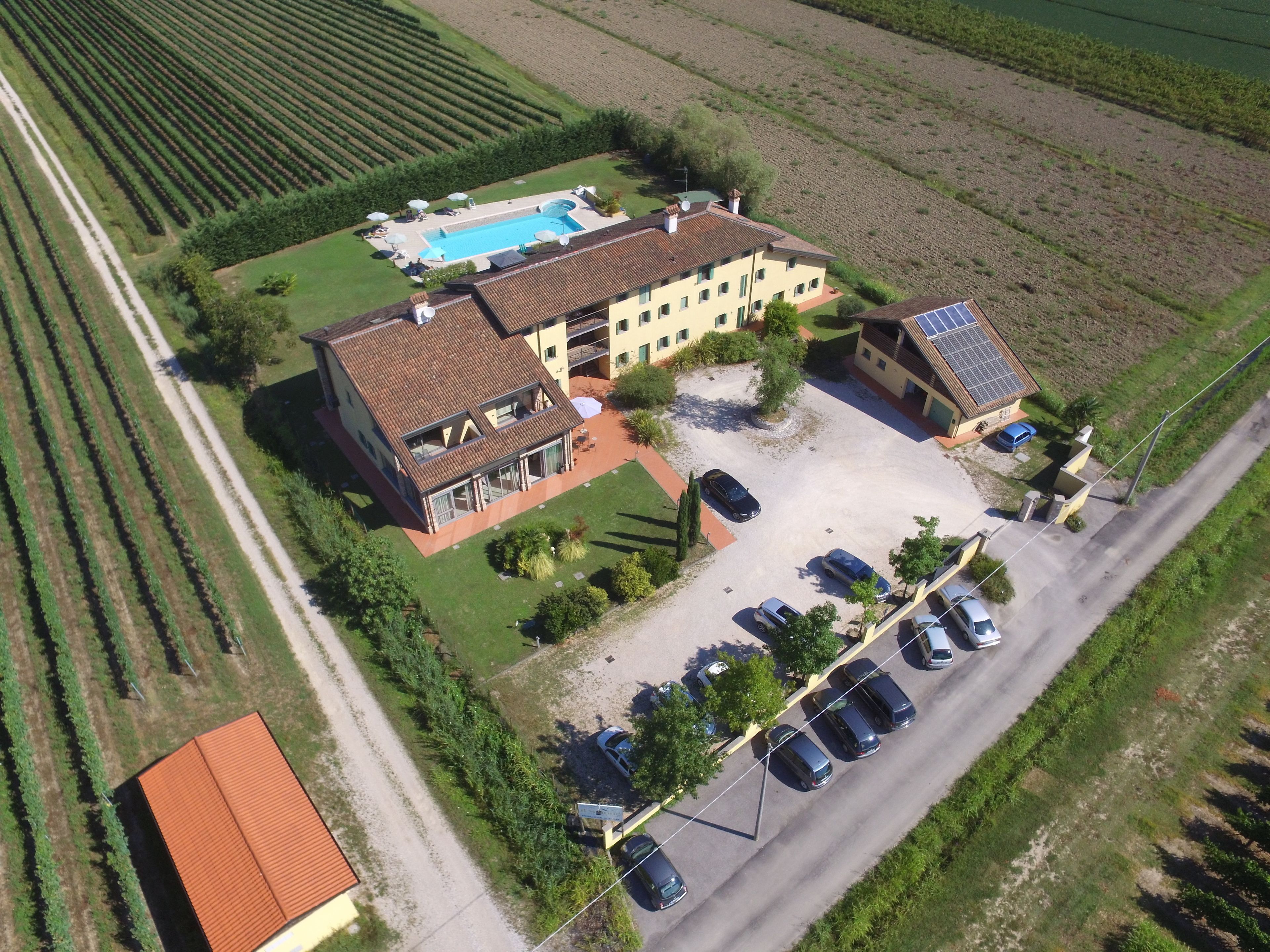 An aerial view of a residential property with a swimming pool, multiple cars, and a solar panel on the roof.