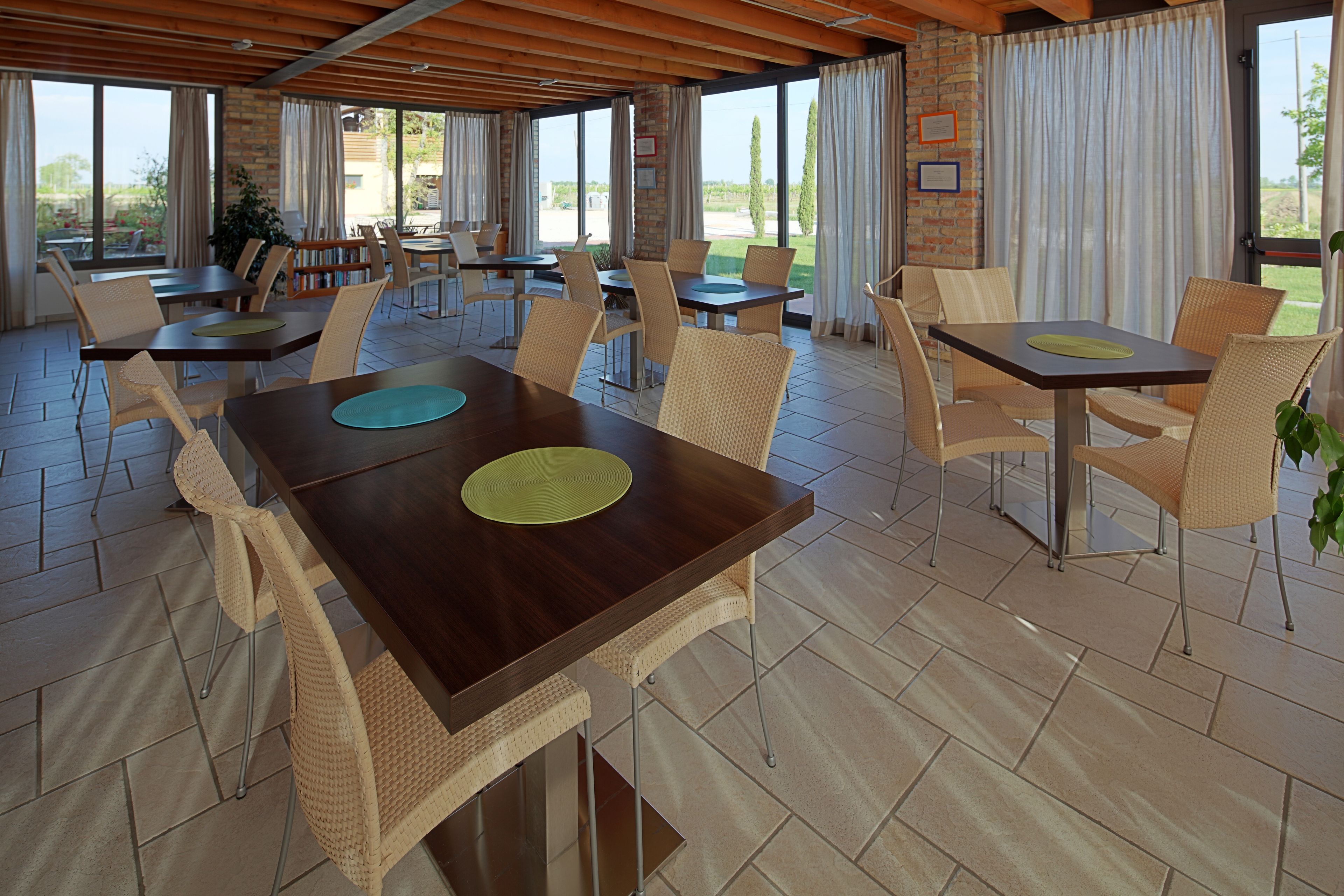 Un amplio espacio comedor al aire libre con varias mesas y sillas, ventanas grandes y vistas del exterior.
