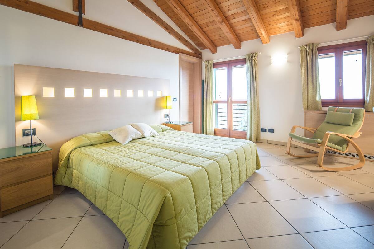 Une chambre avec un lit, deux lampes de chevet, un fauteuil à bascule et une fenêtre avec des rideaux.