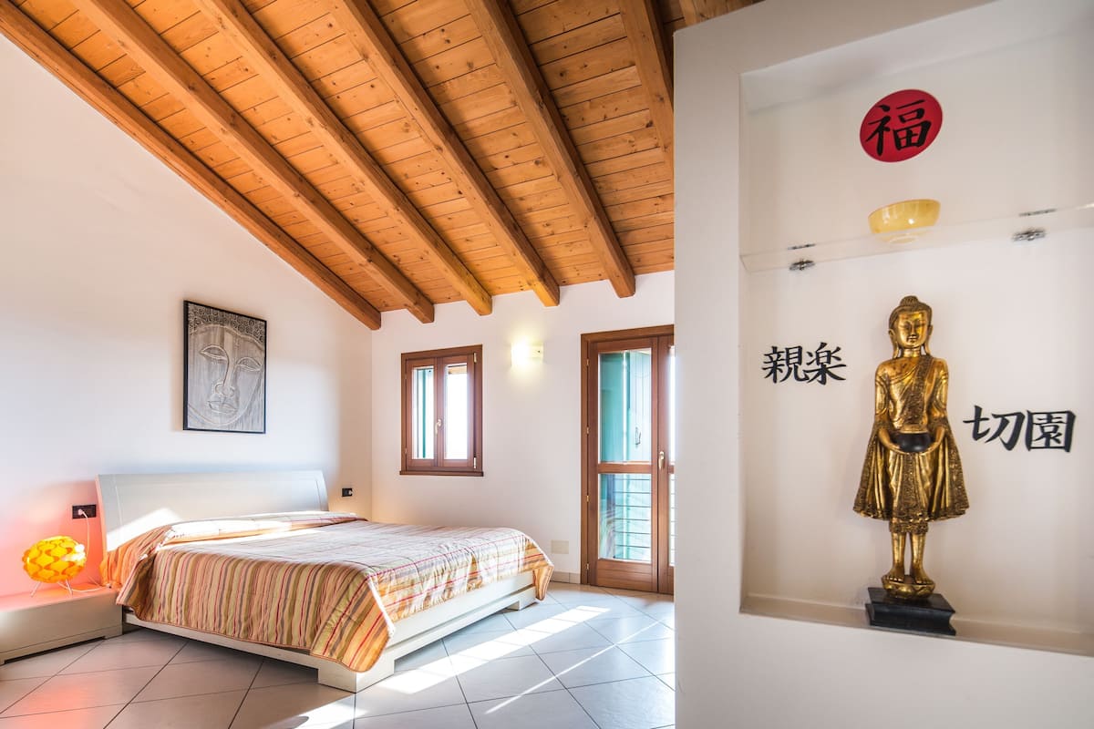 Une chambre à coucher avec un lit, des poutres en bois au plafond, une fenêtre et une statue accrochée au mur.