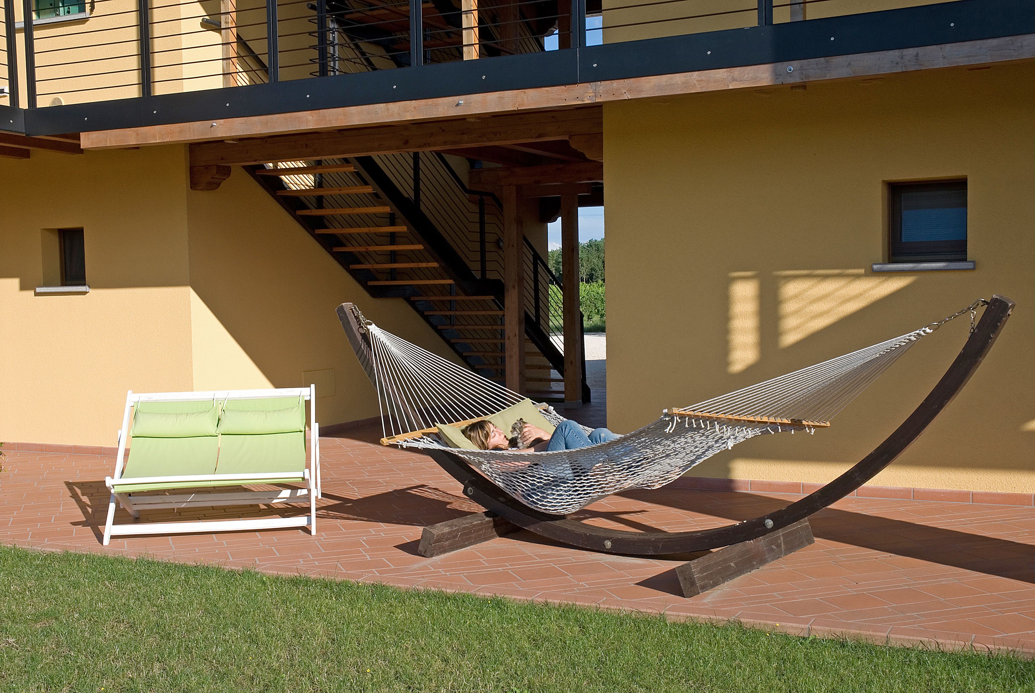 A hammock and a bench in an outdoor area with a brick floor and a yellow wall.