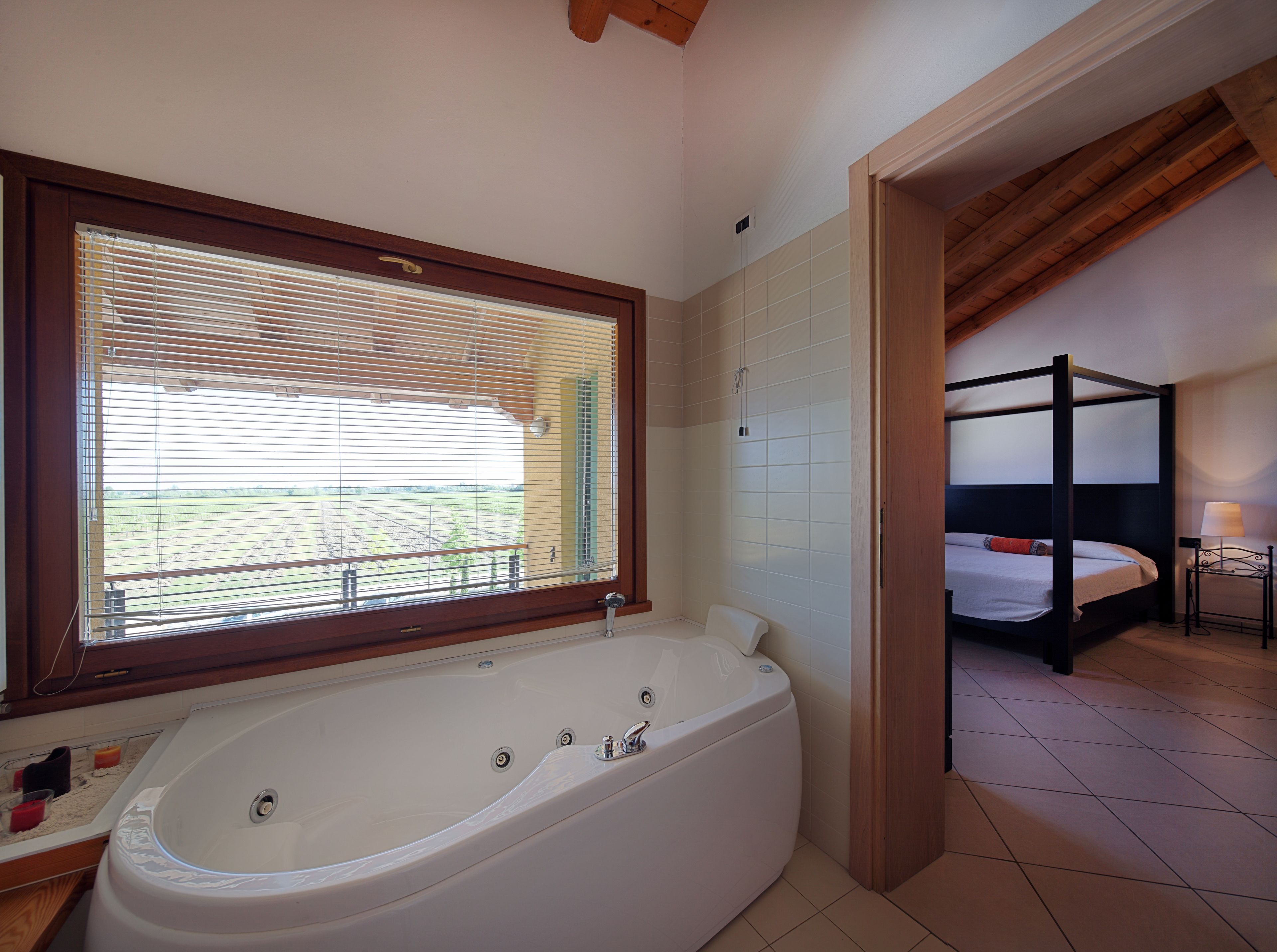 A bathroom with a large bathtub, a window with blinds, and a view of a field.